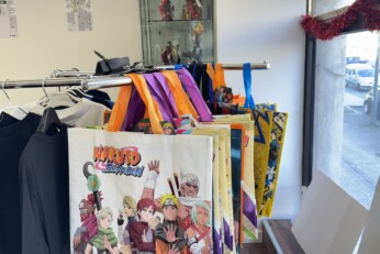 Présentation de divers goodies et accessoires inspirés de mangas, incluant des chapeaux, sacs, figurines et objets de collection, dans une boutique à Cahors.